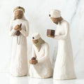 Set of three wiseman figurines -two are standing - far right one standing is holding brown box - one is sitting in the middle holding a rock