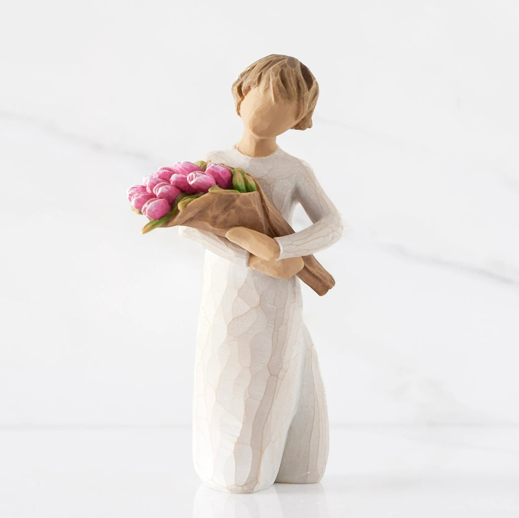 Front view of standing figure in cream dress holding bouquet of pink tulips