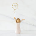Front view: standing figure in cream dress, arms raised, holding gold wire balloon with 2025 written in gold wire inside