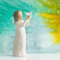 Willow Tree Soar, 5”h hand-painted standing figure in cream dress holding white dove in outstretched hands, in front of teal painting