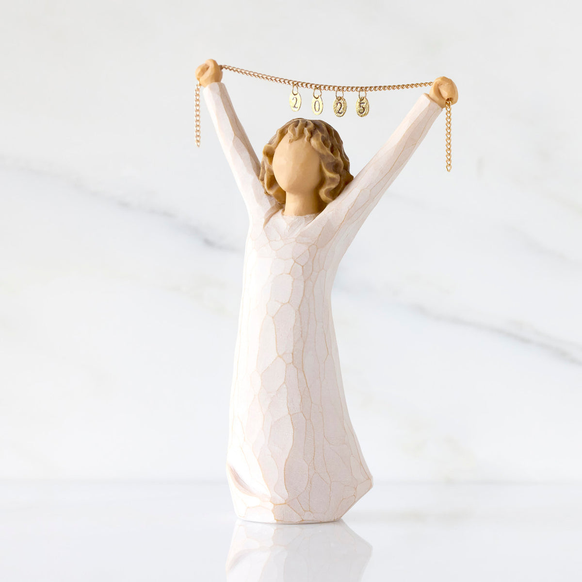 Front view: figure in cream dress holding gold chain above her head with year 2025 on it