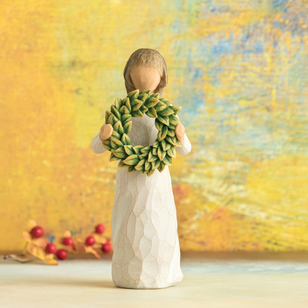 Willow Tree Magnolia, 5.5”h hand-painted standing resin figure in cream dress, holding green magnolia leaf wreath, in front of dark yellow painting