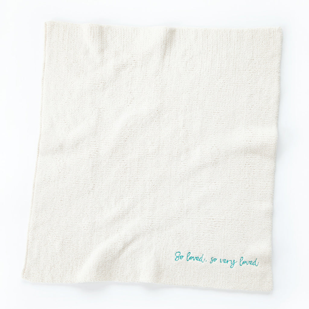 Overview of white towel with 'so loved, so very loved' in light blue in the right corner