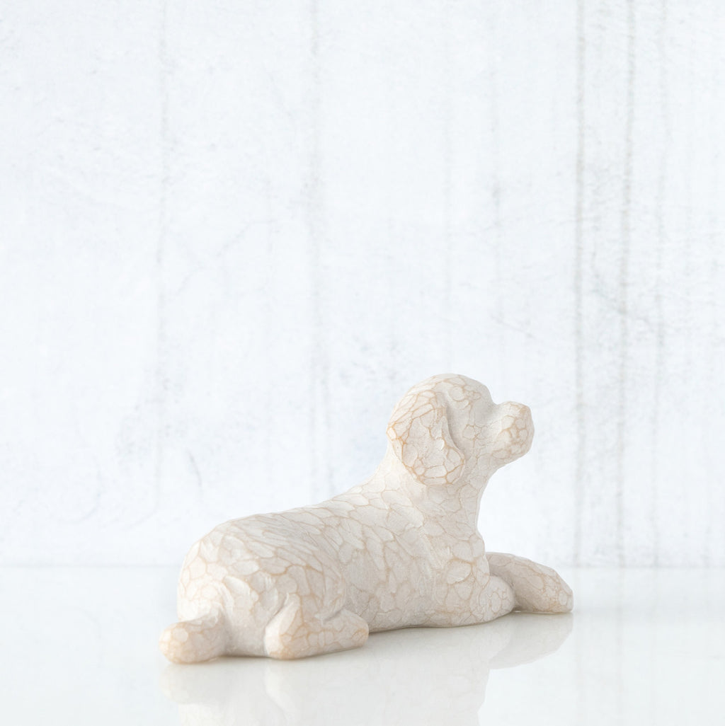 Figure of small white dog laying down with paws crossed in front, facing right