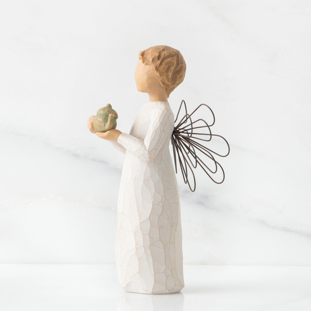Angel figurine in white with black wings facing the side holding golden teapot figurine