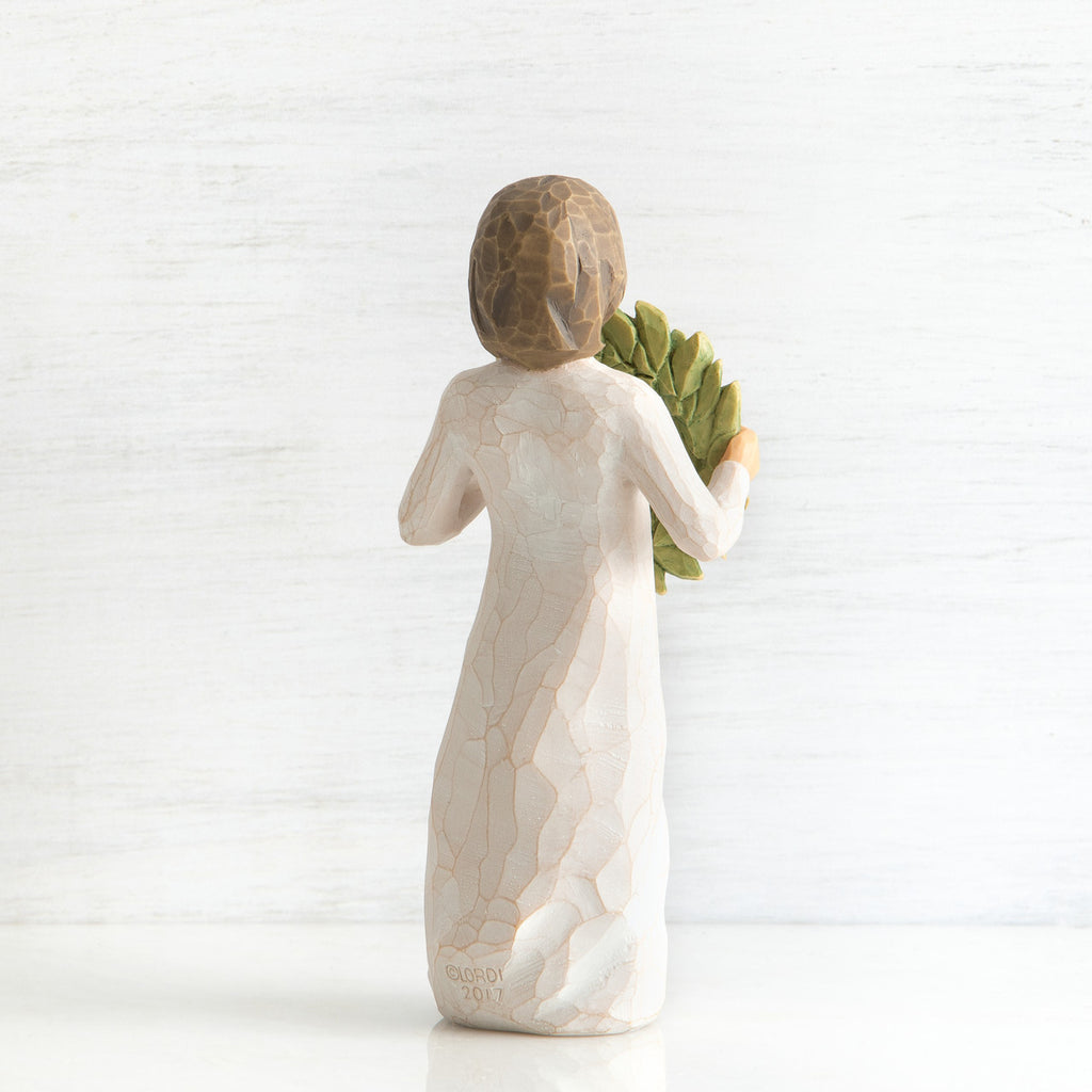 Back view of young girl with bangs and short brown hair holding up a green, leafy wreath