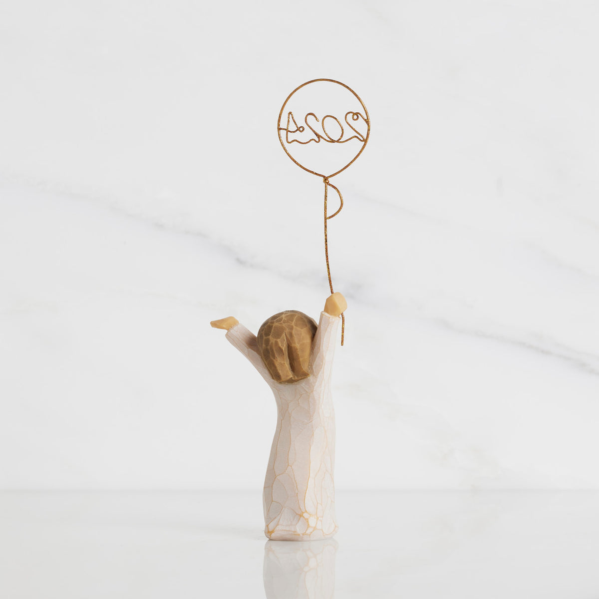 Back view: standing figure in cream dress, arms raised, holding gold wire balloon with 2024 written in gold wire inside