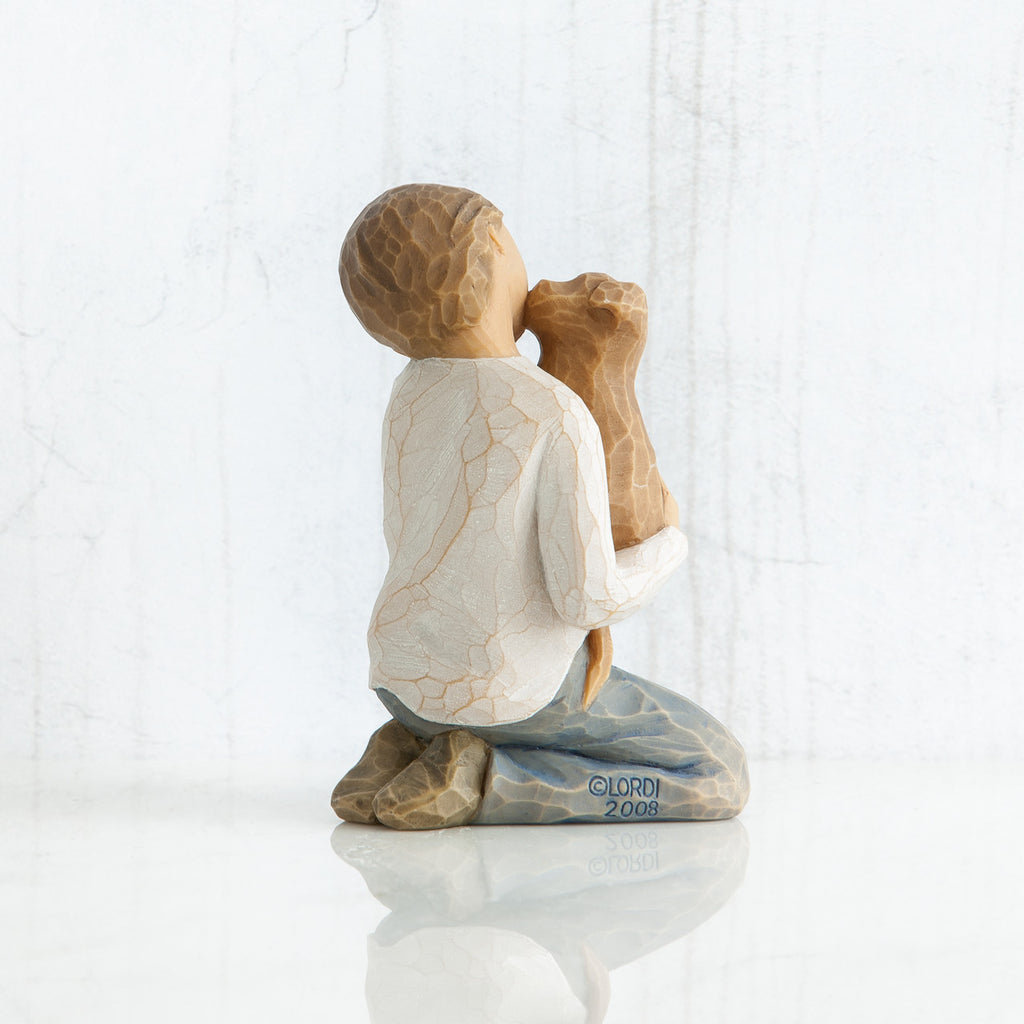 Back view of boy with light brown hair wearing white shirt and jeans and holding a light brown puppy as it licks his face.