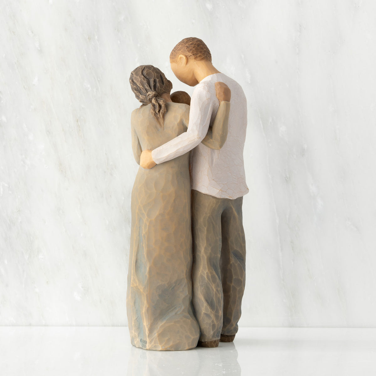 Back view of standing couple, woman has darker skin and hair; man has lighter skin and hair, holding a baby between them.