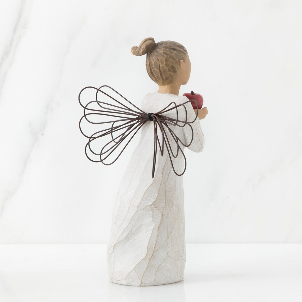 Back view of angel with brown hair in high pony tail leaning forward and holding a red apple up to her face with both hands