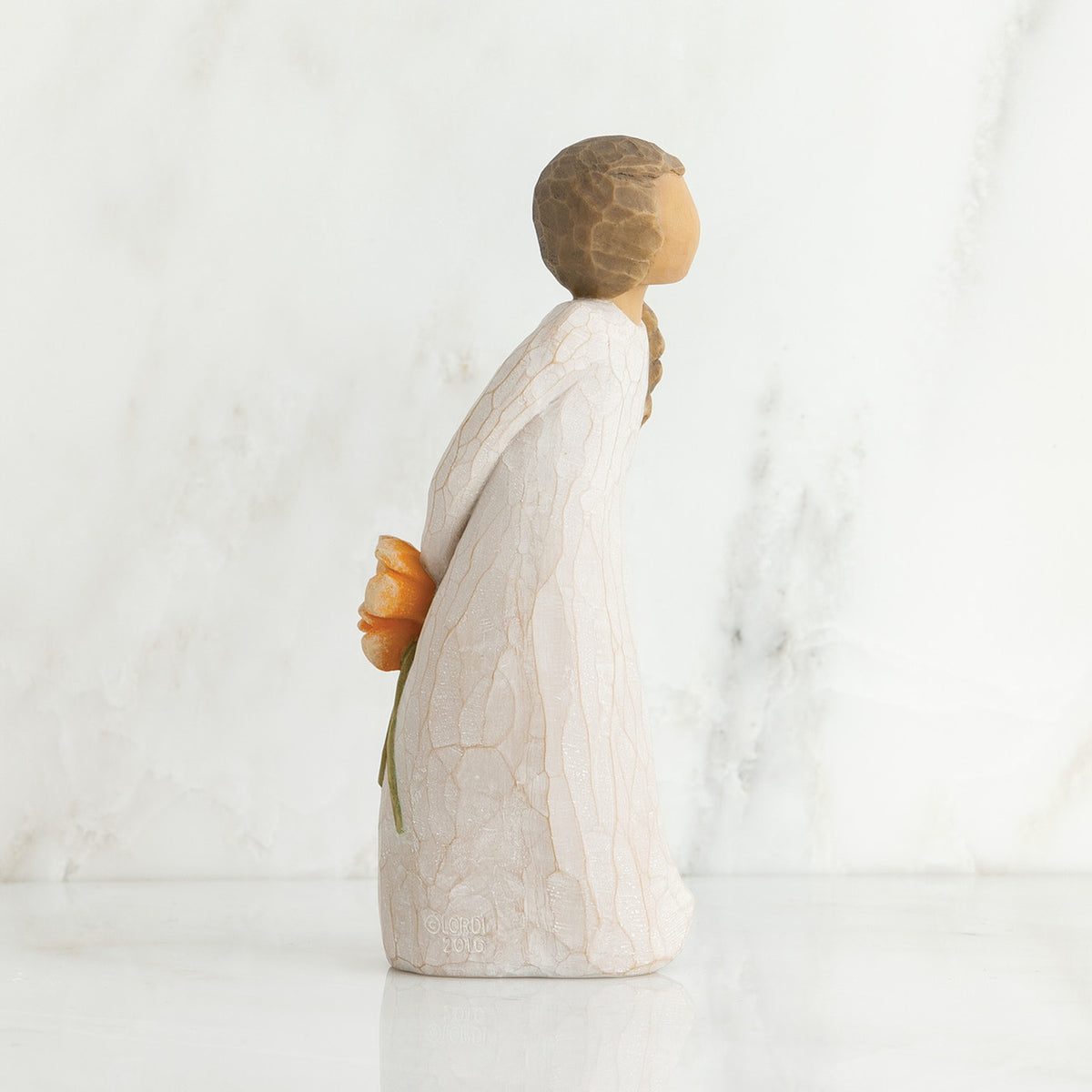 Left side view of girl with brown hair in braid over right shoulder leaning forward as she holds orange flowers behind her back