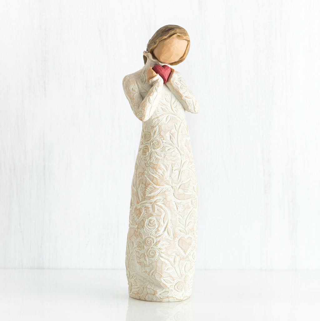 Standing faceless woman figurine in white dress facing forward holding pink heart
