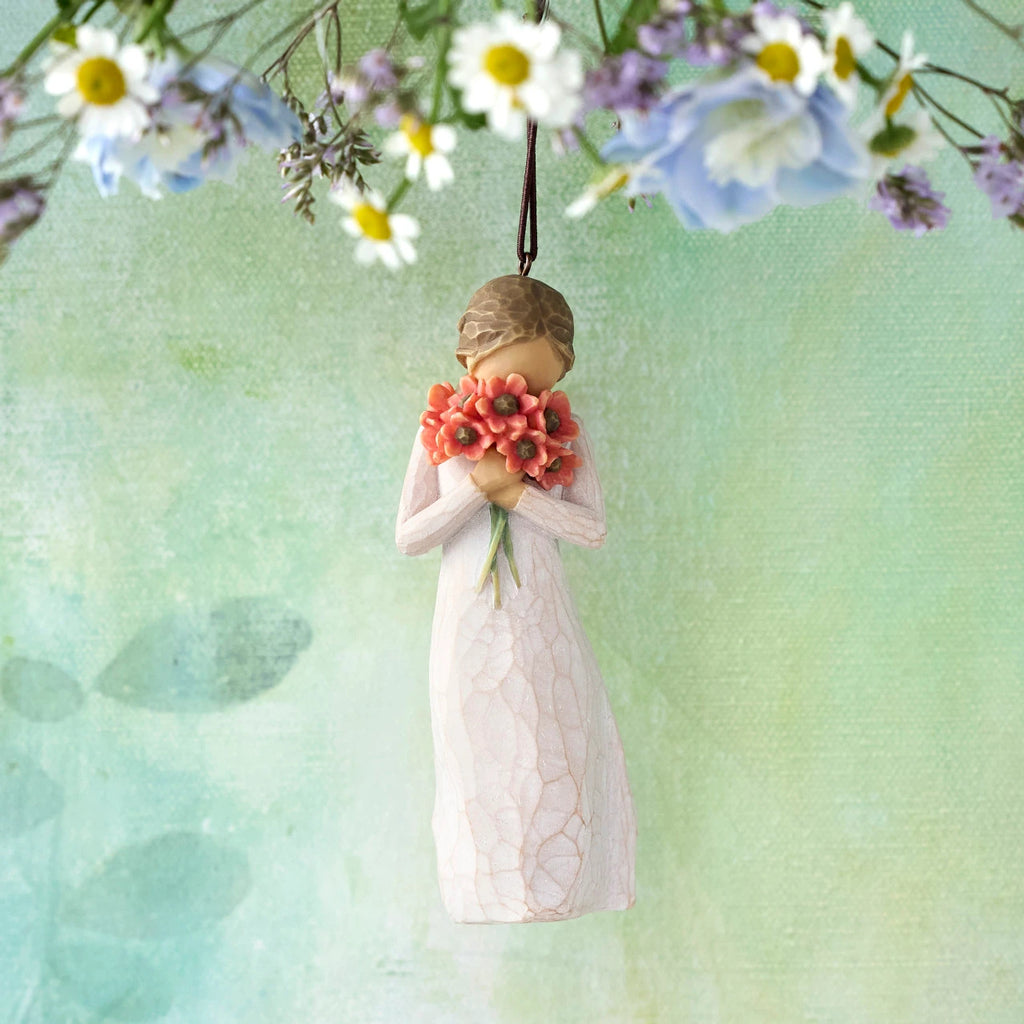 Willow Tree Surrounded by Love Ornament, 4”h hand-painted resin figure in cream dress holding bouquet of poppies to face, brown elastic cord, hanging in front of pale green painting