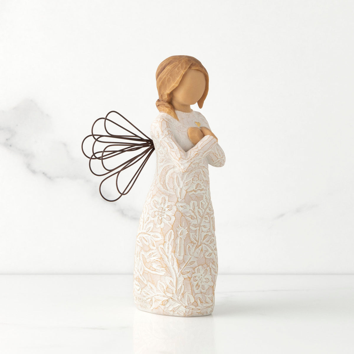 Right side view of standing female figure with wire wings in cream dress carved with natural symbols, hands crossed under gold heart on chest