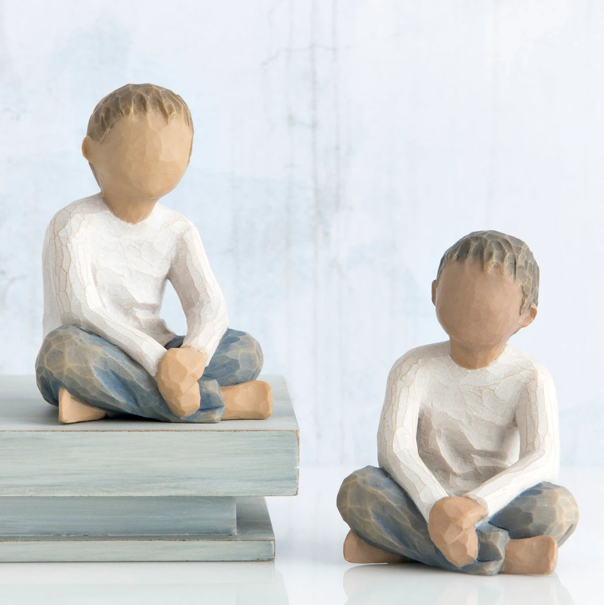 Two young boy figurines sitting next to one another in white shirts and blue jeans