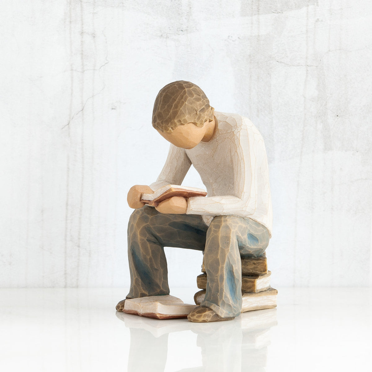 Young faceless boy figurine sitting on books with book opened in his hands - another book on the floor of his feet