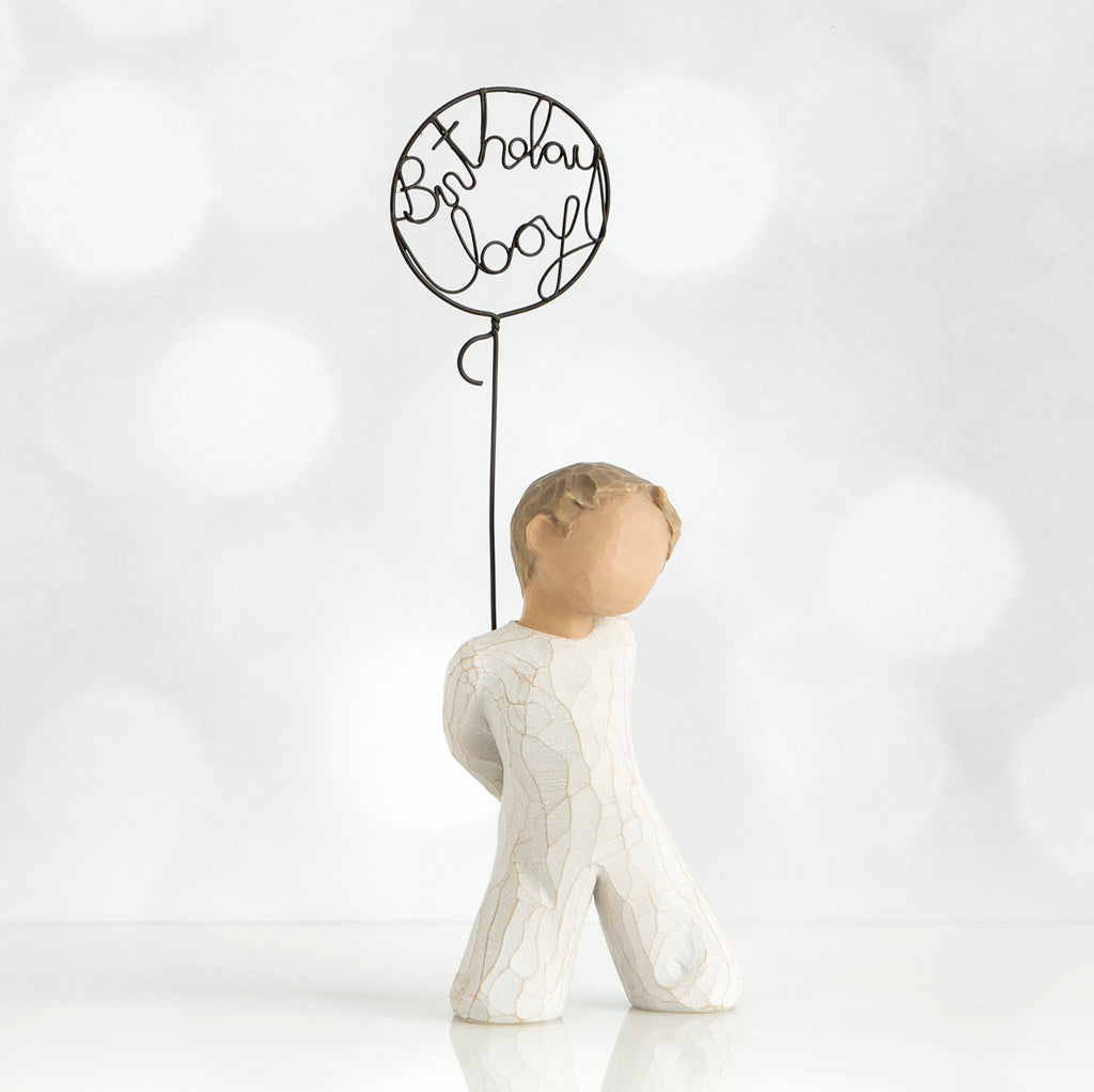 Front view of little boy with light brown hair holding a wire balloon behind his back. Text on balloon is wire