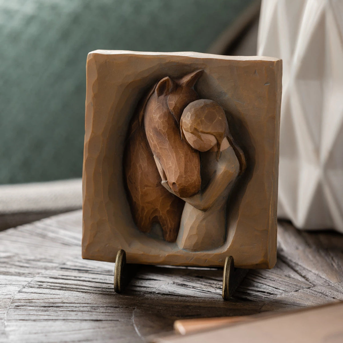 Willow Tree Hug Plaque, 4”sq x .5”d hand-painted resin bas-relief carving of girl in cream dress, arms around neck of reddish-color horse, on green/gray background. Plaque displayed on Plaque Stand on table