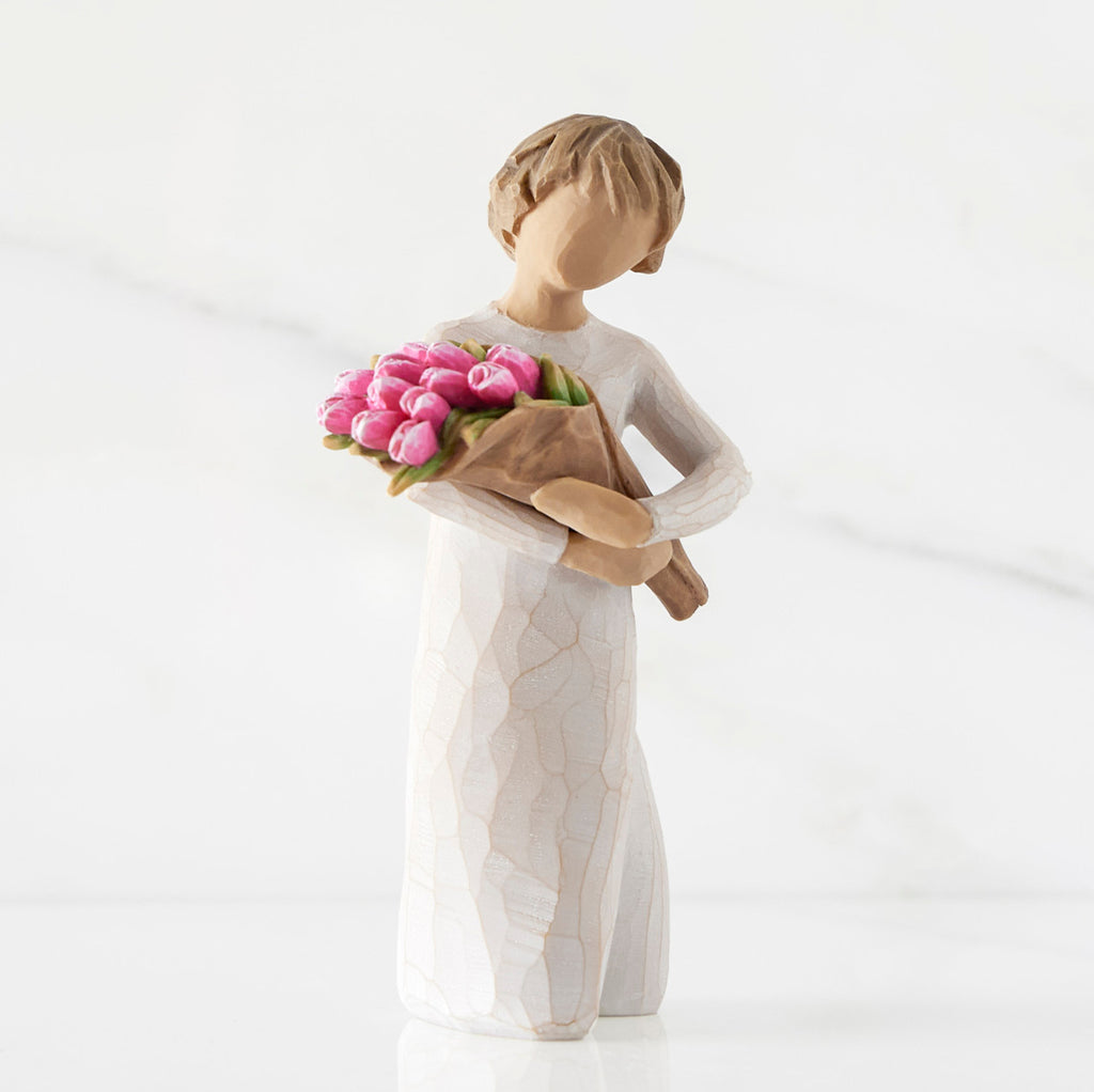 Right side of standing figure in cream dress holding bouquet of pink tulips