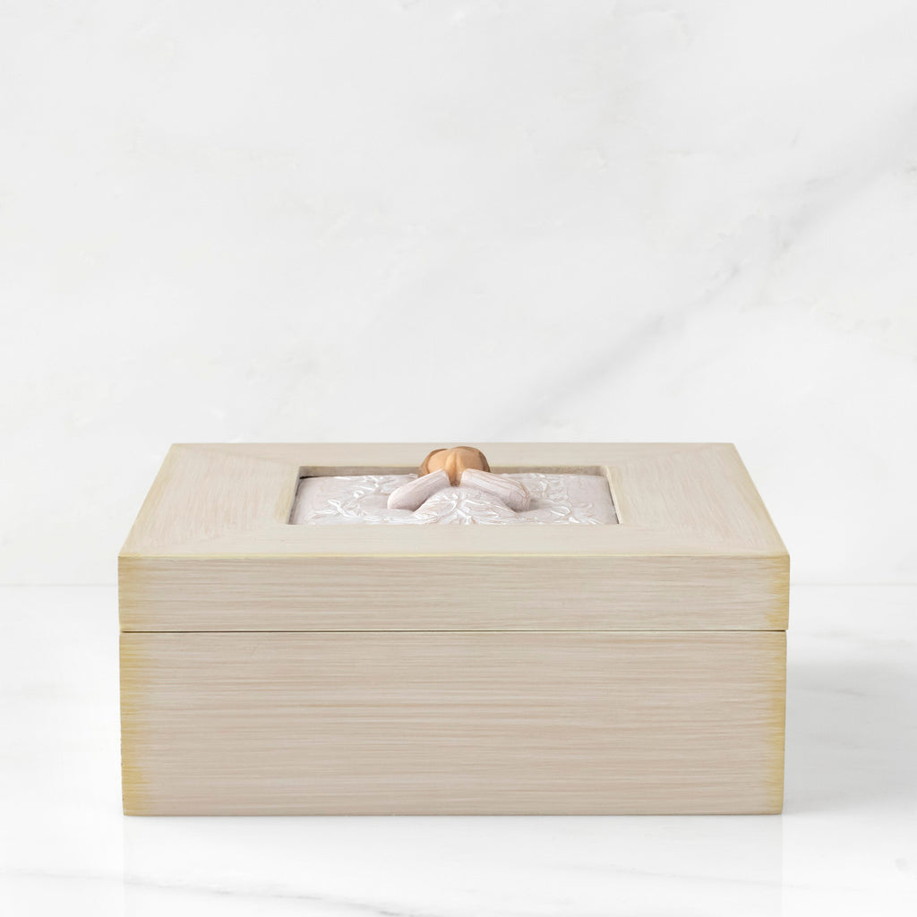 Side View: Cream square wood box with hinged lid, carving on lid of female in cream dress with hands in prayer position, surrounded by leaves and vines
