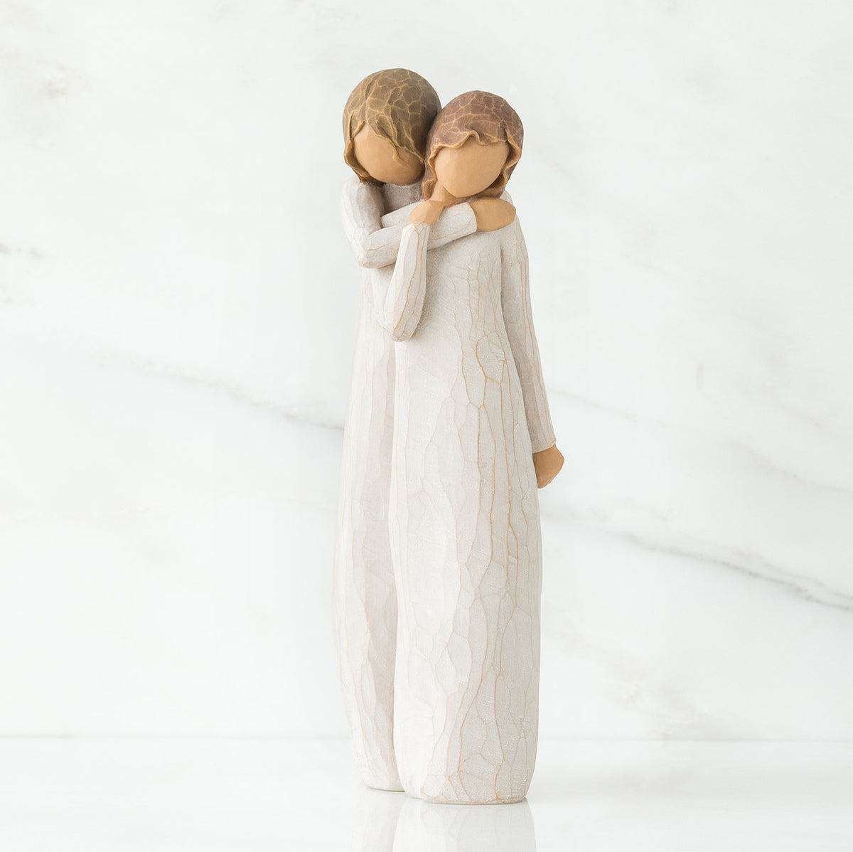 Two faceless woman figurines standing wearing white dresses hugging one another