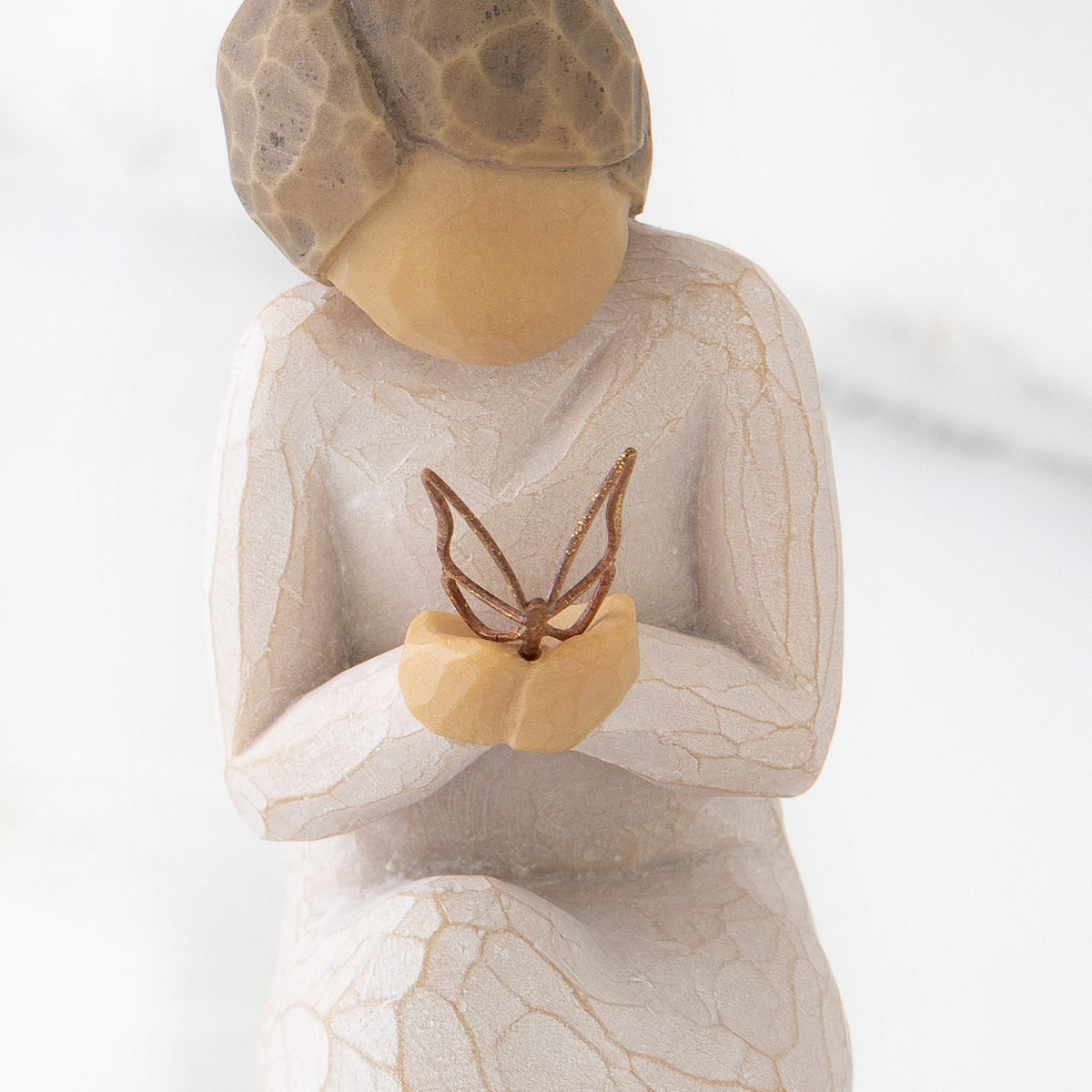 Close up of kneeling female figure in cream dress, holding wire butterfly on extended hands