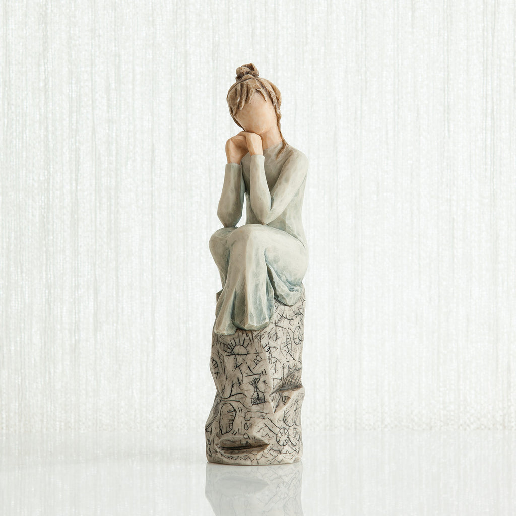 Woman figurine with brown hair in a bun and in white/blue dress sitting on grey printed rock
