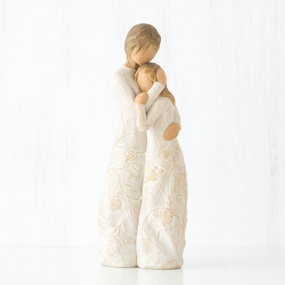 Mother faceless figurine hugging faceless daughter figurine - both standing wearing white dresses