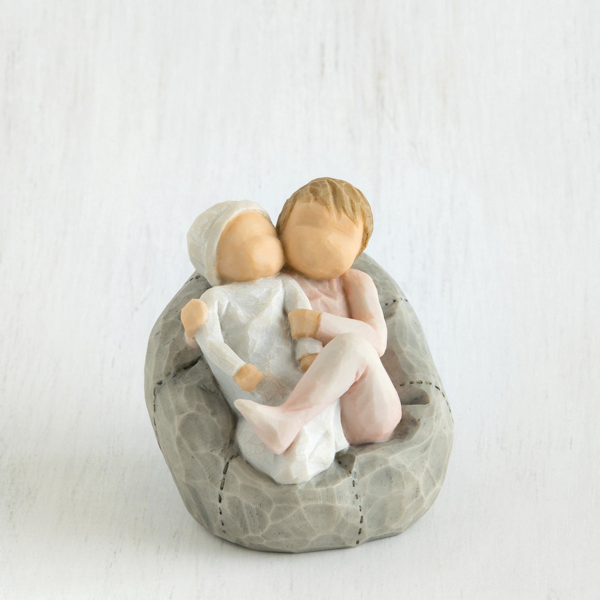 Two small baby figurines hugging another laying on grey beanbag