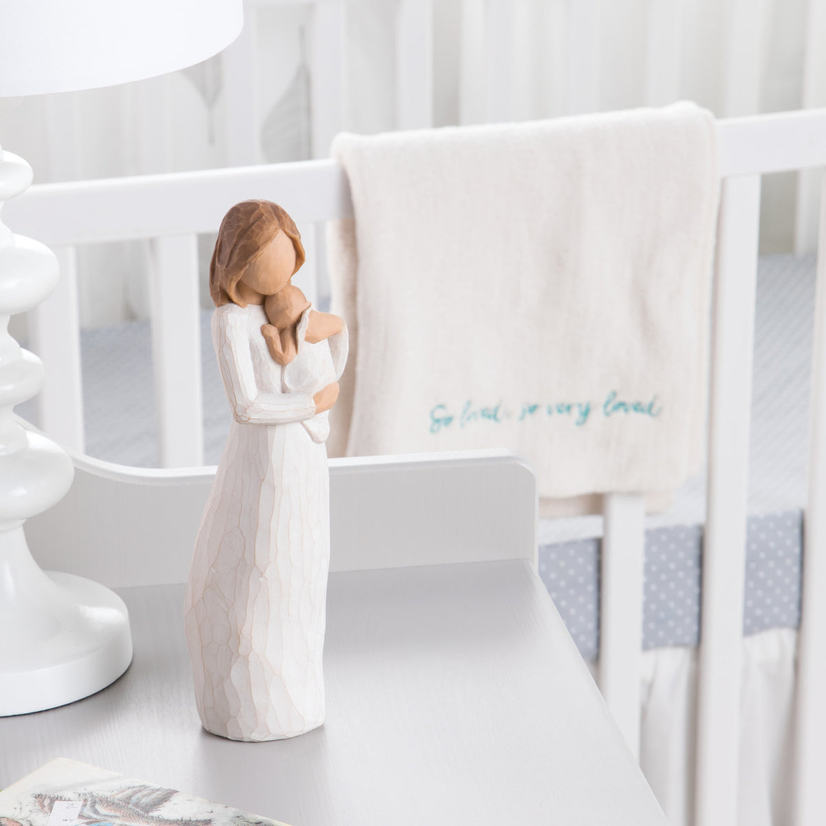 Front view of brunette woman figurine in white dress holding baby on white table