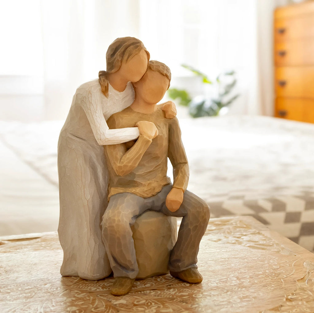 Willow Tree You and Me, 7”h hand-painted resin figure of couple; seated man, woman standing behind with arms around neck, both in neutral clothes, on bedroom table