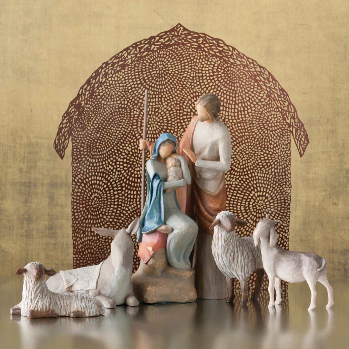 Mary and joesph figurines holding baby with four sheep figurines around them - brown sheer barn paper behind them